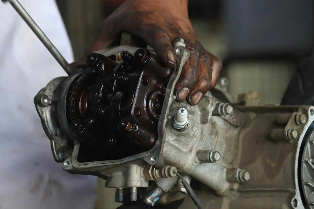 Mechanic's hand repairs engine with screwdriver and spark plug.